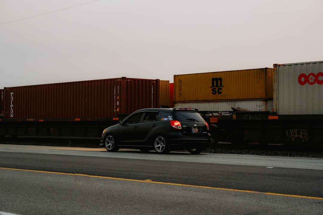 A black car driving down a road next to a train
